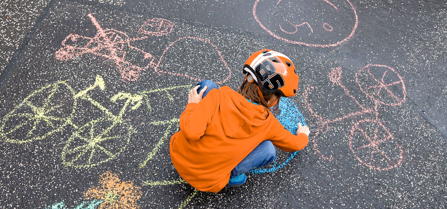 Header Kidical Mass Materialien Ein Kind malt mit Kreide Fahrräder auf die Straße